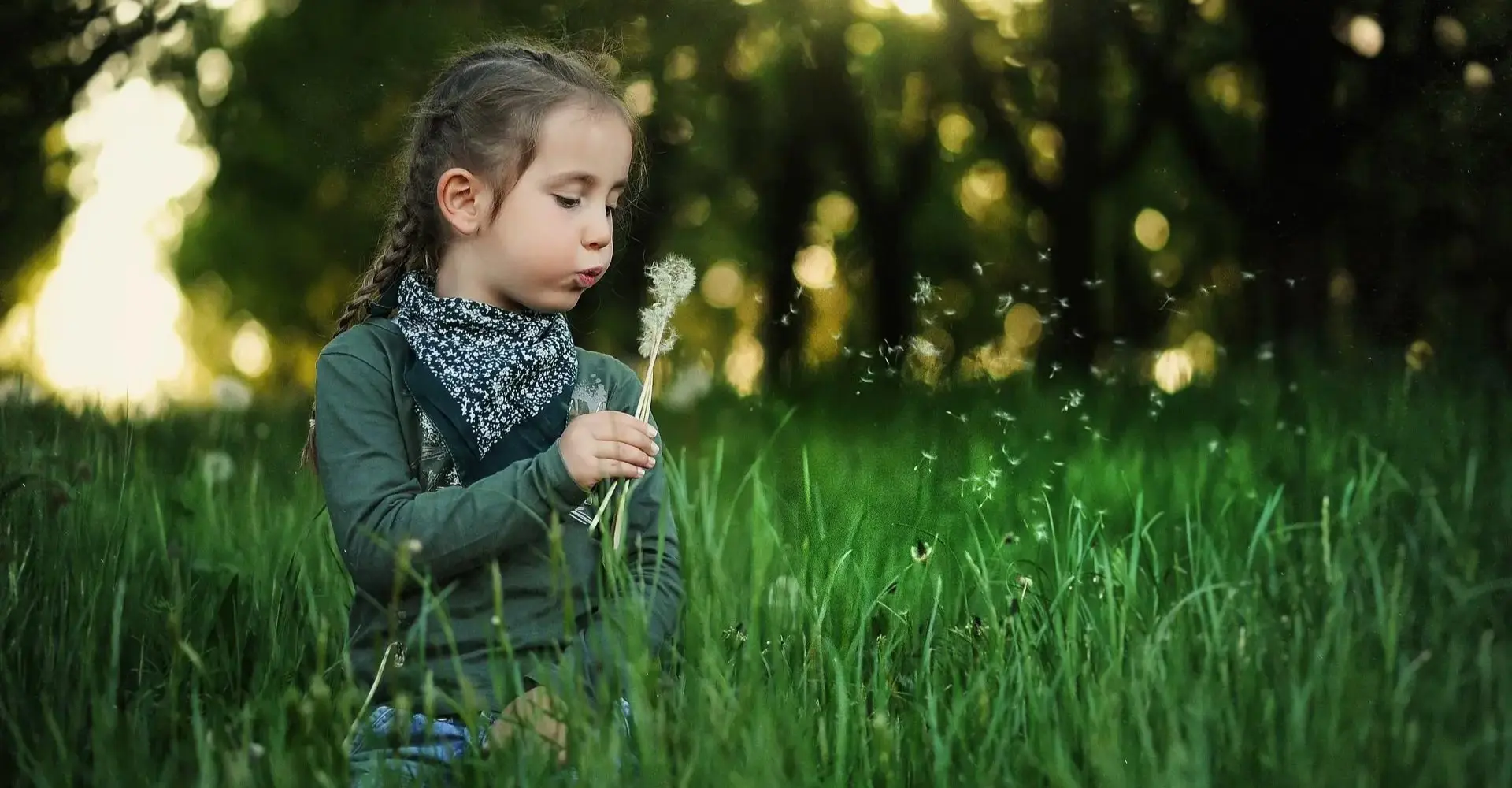 Enfant dans un jardin soufflant sur un pissenlit